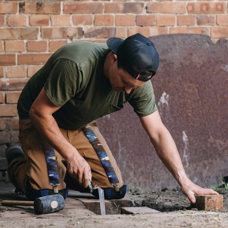 an image of a worker kneeling doing brick paver work to fix a sidewalk