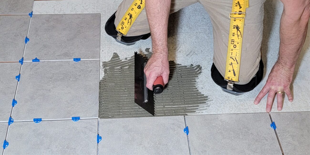Tile installer installing tile wearing knee pad hangers to hold up his knee pads.